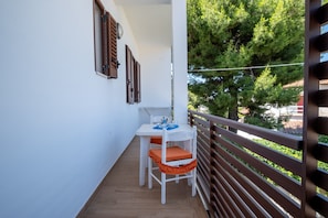 Een balkon met een tafel en stoelen, een leuning en uitzicht op bomen en gebouwen.