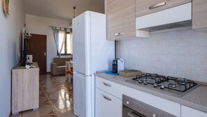 A kitchen with a refrigerator, stove, and a small seating area with a sofa and chair.