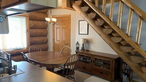A log cabin interior with a dining table, chairs, a kitchen area, a staircase, and a bookshelf. - Fence Lake Condo #10 - Docking, Wifi, Beach (Lac du Flambeau)