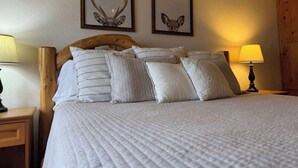 A bed with a wooden headboard, multiple pillows, two framed deer antlers on the wall, and two bedside lamps. - Fence Lake Condo #10 - Docking, Wifi, Beach (Lac du Flambeau)