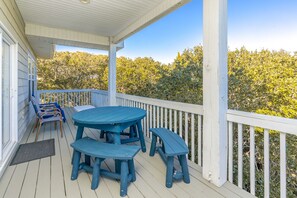 Eine überdachte Terrasse mit Tisch und Bänken, umgeben von einem weißen Geländer, mit Blick auf einen Wald.