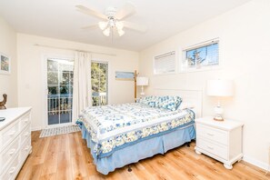 Ein Schlafzimmer mit Bett, Nachttisch, Kommode, Deckenventilator und einem Fenster mit Jalousien.
