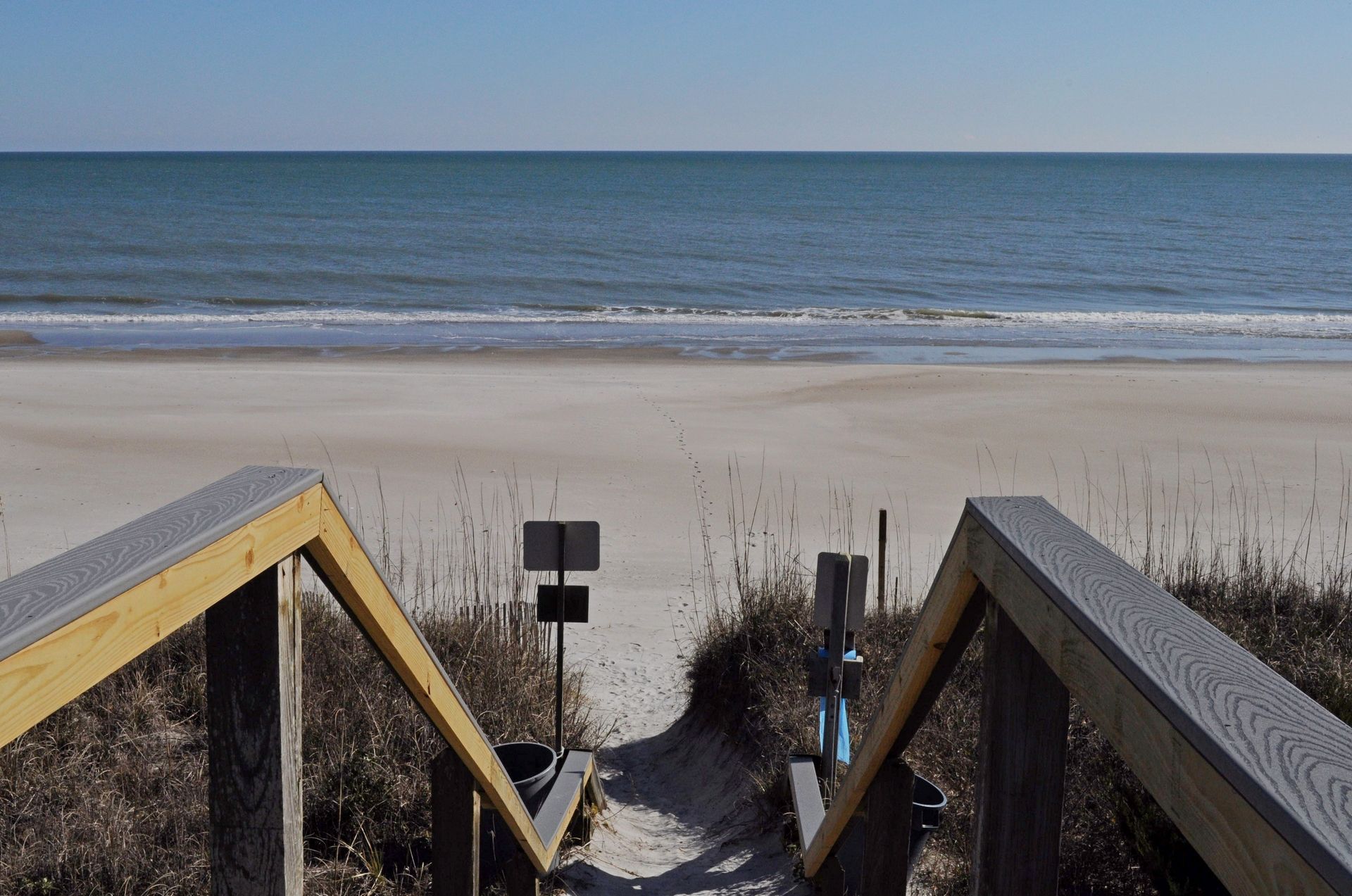 A wooden boardwalk leading to a sandy beach with the ocean in the background.