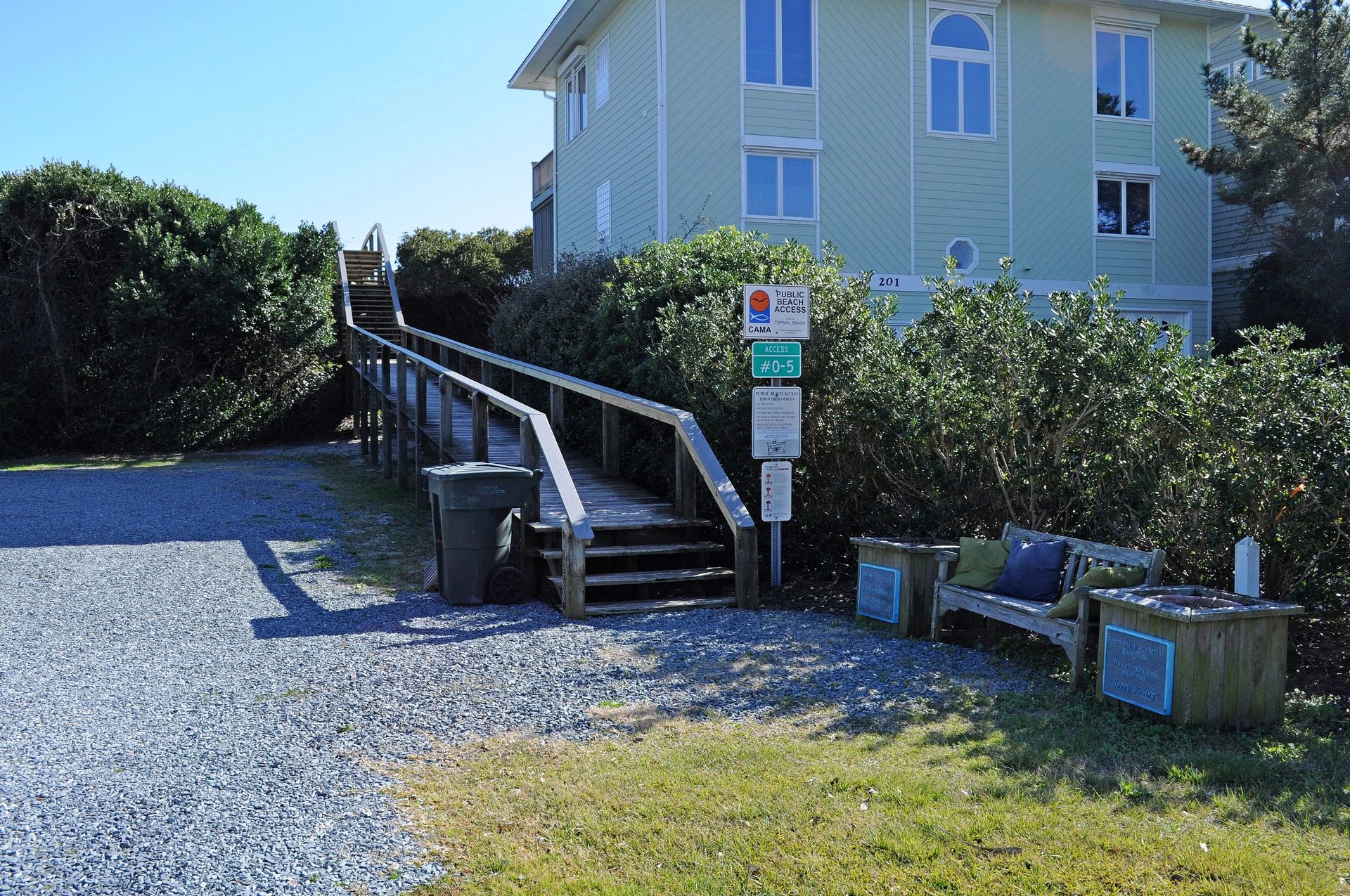 A wooden staircase leading to a building, a trash bin, and a bench with a sign.