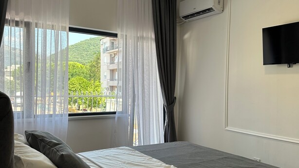 A bedroom with a bed, a window with curtains, an air conditioning unit, and a mounted television.