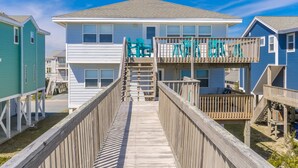 A beachfront property with a wooden boardwalk leading to a two-story building with balconies. - What A View: Oceanfront 6-bedroom home in Surf City perfect for families. (Surf City)