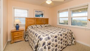 A bedroom with a bed, a nightstand, a lamp, a ceiling fan, and two windows. - What A View: Oceanfront 6-bedroom home in Surf City perfect for families. (Surf City)
