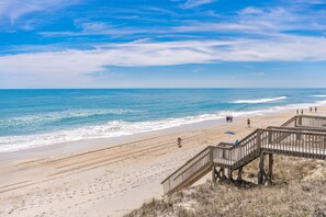 Ein Strand mit einer Holzpromenade, die zum Wasser führt, feinem Sand und einem klaren Himmel.