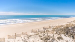Ein Strand mit Holzzaun und Liegestühlen, mit Blick auf den Ozean.