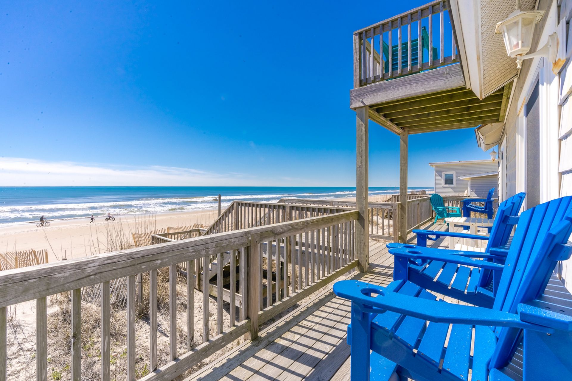 A wooden deck with blue chairs overlooking a beach.