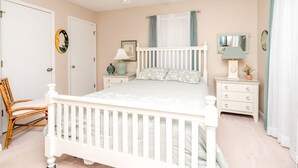 Ein Schlafzimmer mit einem Babybett, einem Nachttisch mit Lampe, einem Sessel und einem Deckenventilator.