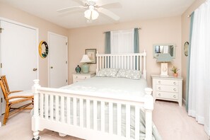 A bedroom with a crib, a bedside table with a lamp, a chair, and a ceiling fan. - Whittington - Oceanfront 3-Bedroom, perfect for family getaways! (North Topsail Beach)