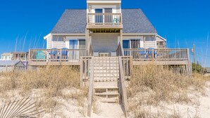 Ein zweistöckiges Strandhaus mit einer Holzterrasse und einer Treppe zum Eingang.