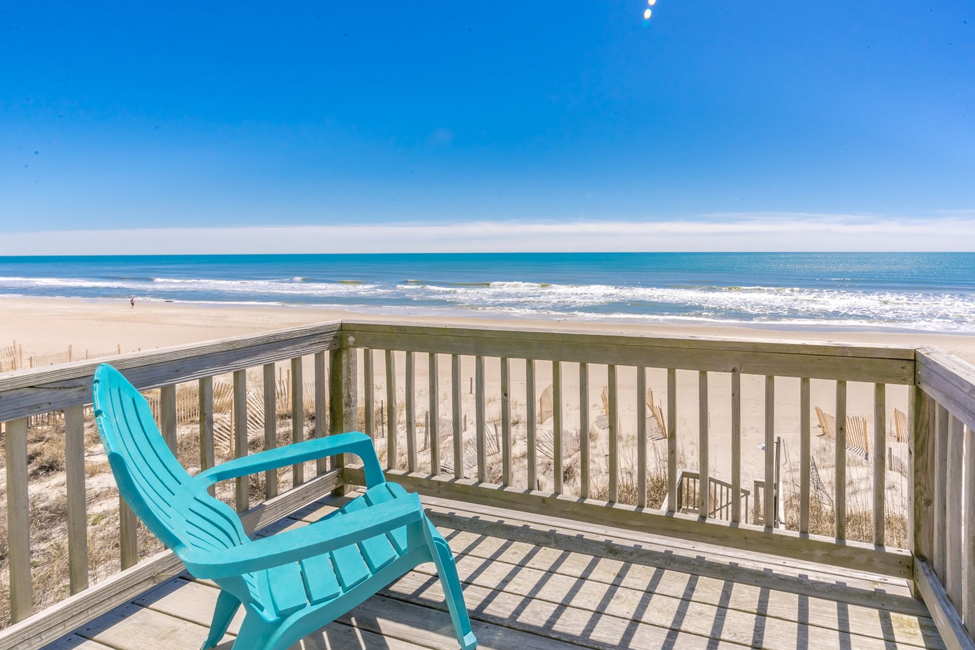 A turquoise Adirondack chair on a wooden deck overlooking a beach with waves.