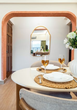 A dining area with a round table, two glasses of wine, and a mirror above. - Staymaster Enchanto 2BR Apartment (Siolim)