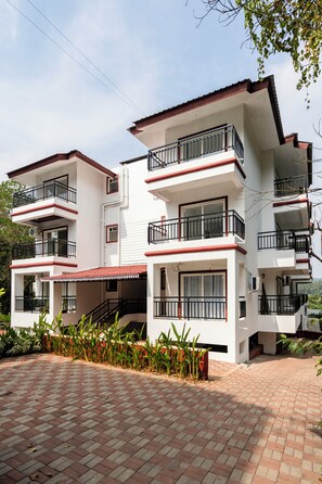 Un edificio residencial de varios pisos, con balcones, techo de tejas rojas y entrada pavimentada.