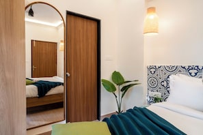 A bedroom with a bed, a mirror, a door, and a wall-mounted light fixture. - Staymaster Enchanto 2BR Apartment (Siolim)