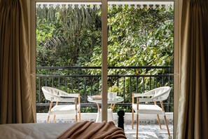 Una habitació amb un llit, una finestra amb cortines i un balcó amb dues cadires blanques i una taula petita.