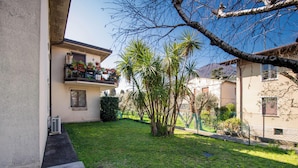 Um edifício residencial com varanda, jardim cercado e céu claro.