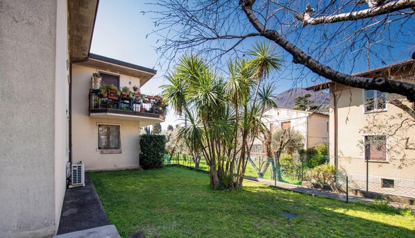 Un edificio residencial con balcón, jardín cercado y cielo despejado.