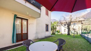 Un patio con una mesa y sillas, un paraguas rojo y un edificio con balcón.