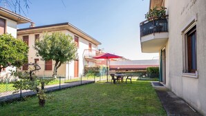 Um pátio com uma mesa, cadeiras, um guarda-sol vermelho e uma pequena árvore.