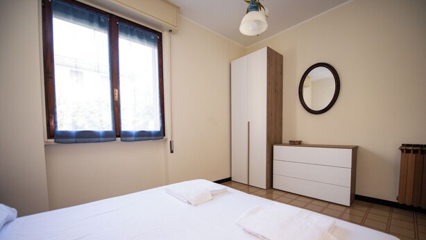 Quarto com cama, penteadeira, espelho e janela com cortinas.
