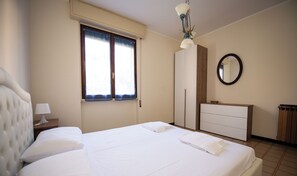 Una habitación de hotel con cama, mesita de noche, cómoda, espejo y ventana con cortinas.