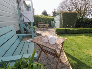 A wooden deck with a table and chairs, a small garden area with a hedge, and a building with a door and window. - Higher Merther Farm Shepherds Hut (Helston)