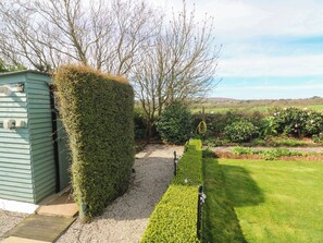 Ein Gartenweg führt zu einem Gartenhaus, umgeben von gepflegten Hecken und einer Rasenfläche.