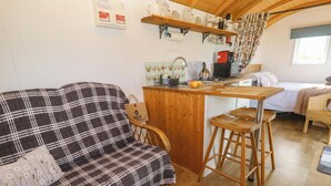 A cozy room with a plaid sofa, a wooden bar area, and a bed with a patterned bedspread. - Higher Merther Farm Shepherds Hut (Helston)