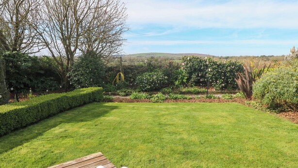 A garden with a wooden table, a white teapot, and a plate of food. - Higher Merther Farm Shepherds Hut (Helston)