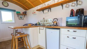 A compact kitchen with a wooden bar stool, a small refrigerator, a microwave, and a sink. - Higher Merther Farm Shepherds Hut (Helston)