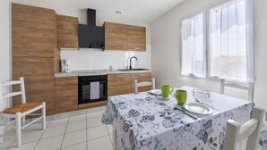 Une cuisine moderne avec des meubles en bois, une table à manger recouverte d’une nappe à motifs floraux et une fenêtre agrémentée de rideaux légers.