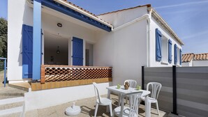 Un bâtiment blanc avec des volets bleus, une terrasse avec des chaises et une table blanches, et une clôture en bois.