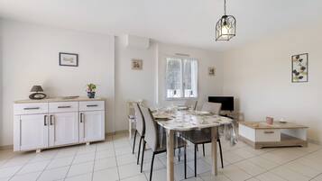 Un comedor con una mesa lista para cuatro, un armario con cajones, un televisor y una ventana con cortinas.