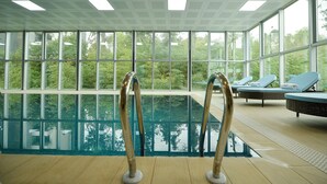 An indoor swimming pool with clear glass walls, a tiled ceiling, and lounge chairs with towels. - Calligraphy Hotel (Batumi)