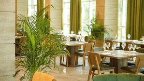 A restaurant with tables set for dining, chairs, and potted plants. - Calligraphy Hotel (Batumi)