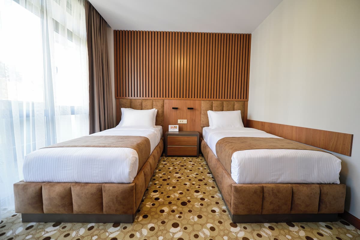 Ett hotellrum med två sängar, en sänggavel i trä, en mönstrad matta och ett fönster med gardiner.