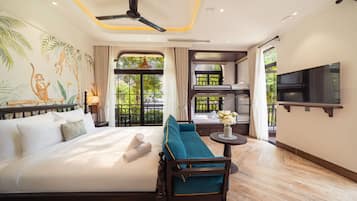 Quarto de hotel com cama, sofá, televisão e varanda com vista para área verde.