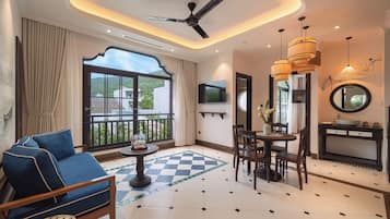 Habitación de hotel con balcón, zona de comedor y televisor montado en la pared.