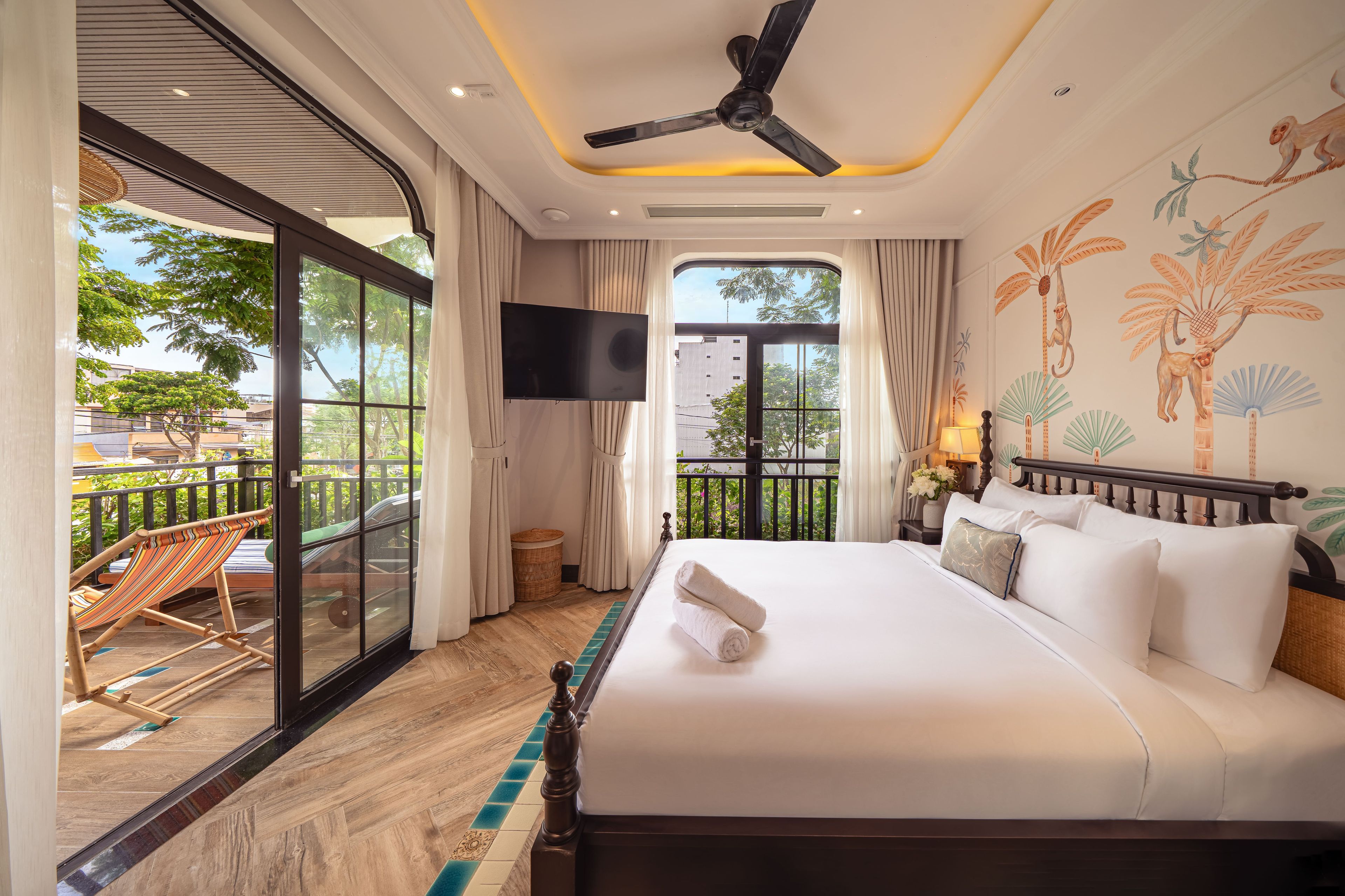 A hotel room with a bed, a television, a balcony with a chair, and a view of the outside.