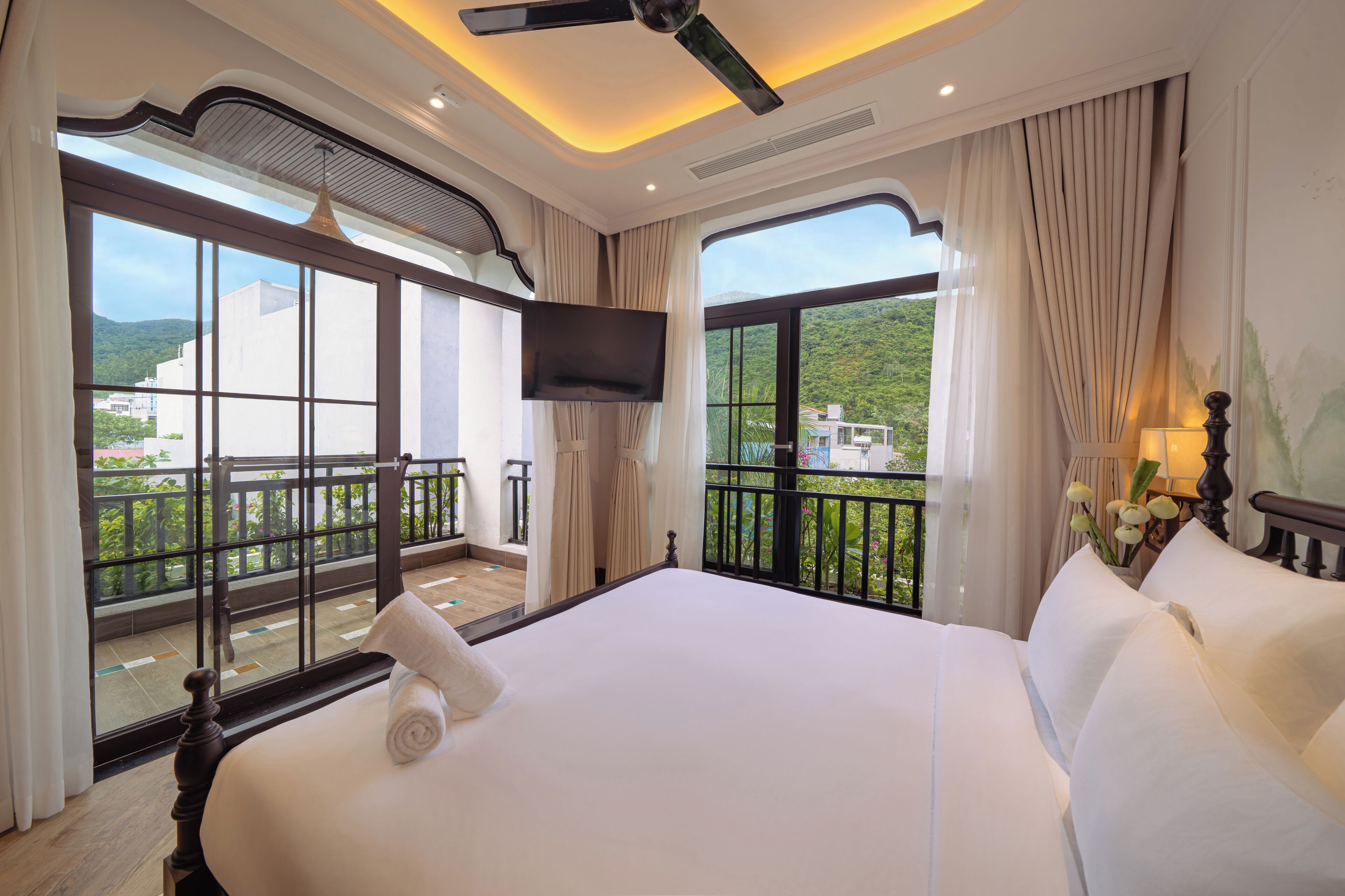 Ein Hotelzimmer mit einem großen Bett, einem flachbildfernseher an der Wand und einem Balkon mit Blick auf Grünflächen und Gebäude.