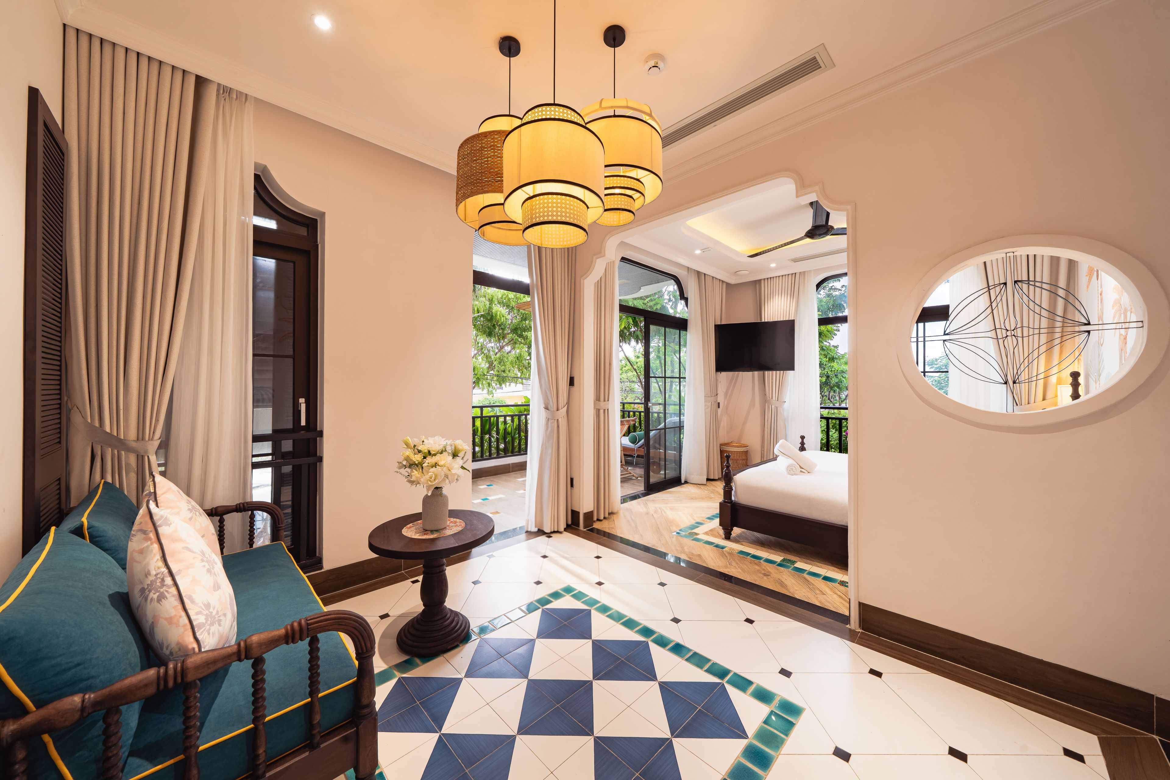 Une chambre d’hôtel avec un sol à carreaux, un lit, un canapé, une table avec un vase de fleurs et une grande fenêtre avec des rideaux.