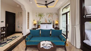 A hotel room with a sofa, a ceiling fan, a bed, a nightstand, a lamp, and a window with curtains. - Natalie Indochine Mountain Villa Da Nang (Da Nang)