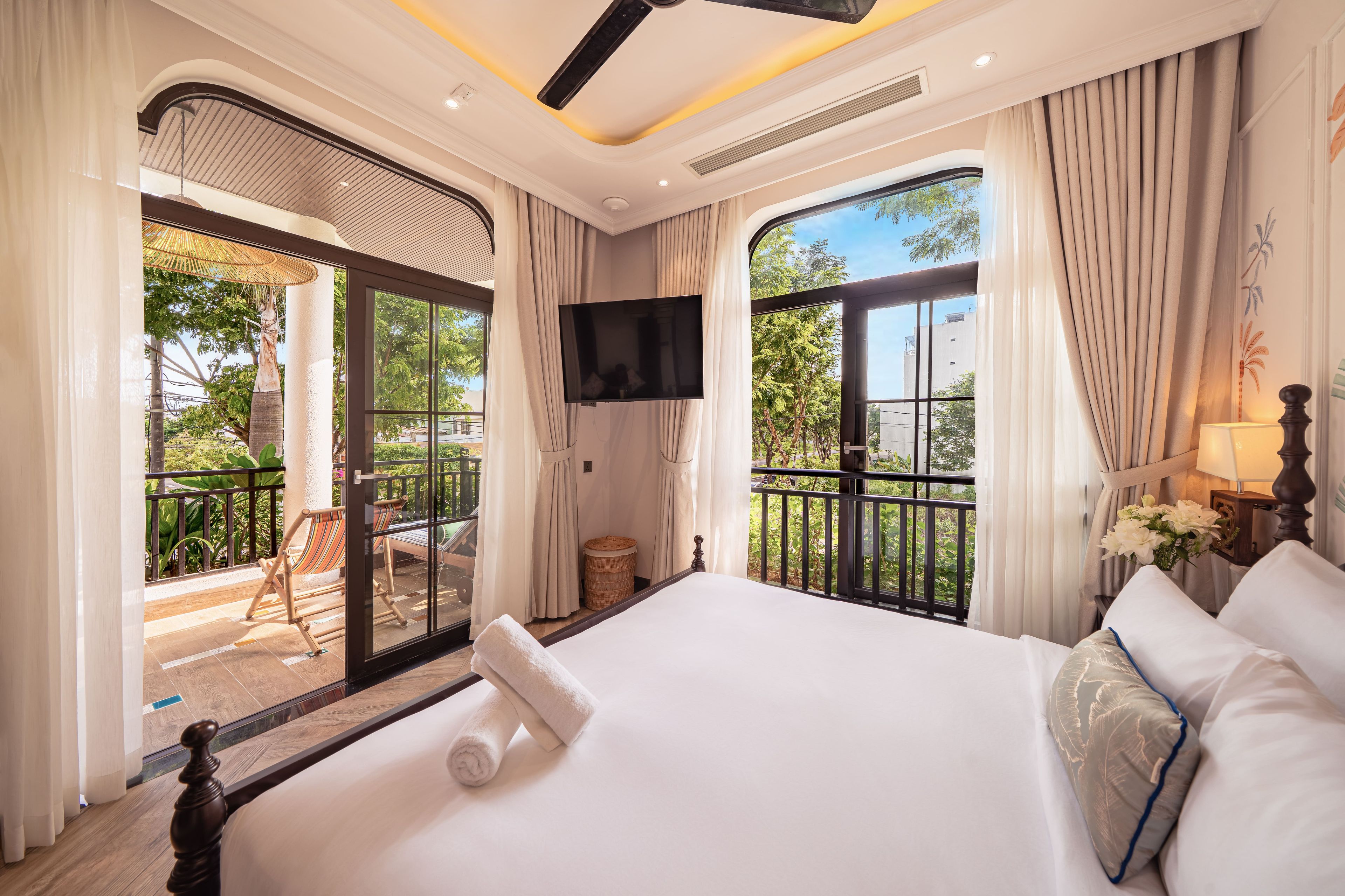 A hotel room with a large bed, a TV, a balcony with a chair, and curtains.