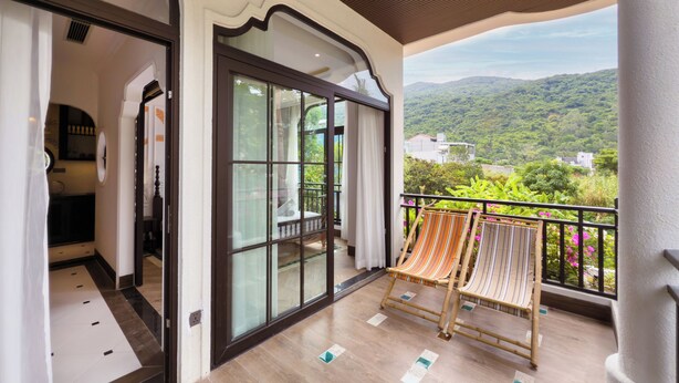 A balcony with a view of a green landscape, a sliding glass door, and a chair. - Natalie Indochine Mountain Villa Da Nang (Da Nang)