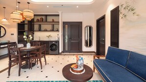A modern living room with a blue sofa, a dining table with chairs, a coffee table, and a kitchen area with a washing machine. - Natalie Indochine Mountain Villa Da Nang (Da Nang)
