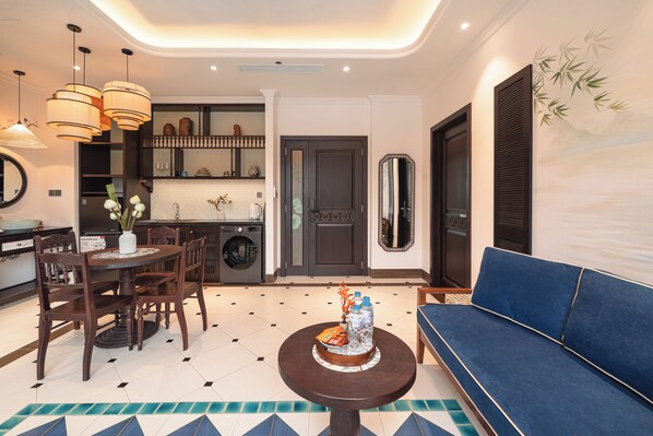 Una sala moderna con un sofá azul, una mesa de comedor con sillas, una mesa de centro y una zona de cocina con lavadora.