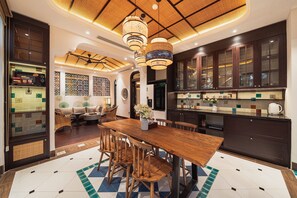 A modern kitchen with dark cabinets, a wooden dining table, and a patterned floor. - Natalie Indochine Mountain Villa Da Nang By Sujet of Haviland (Da Nang)